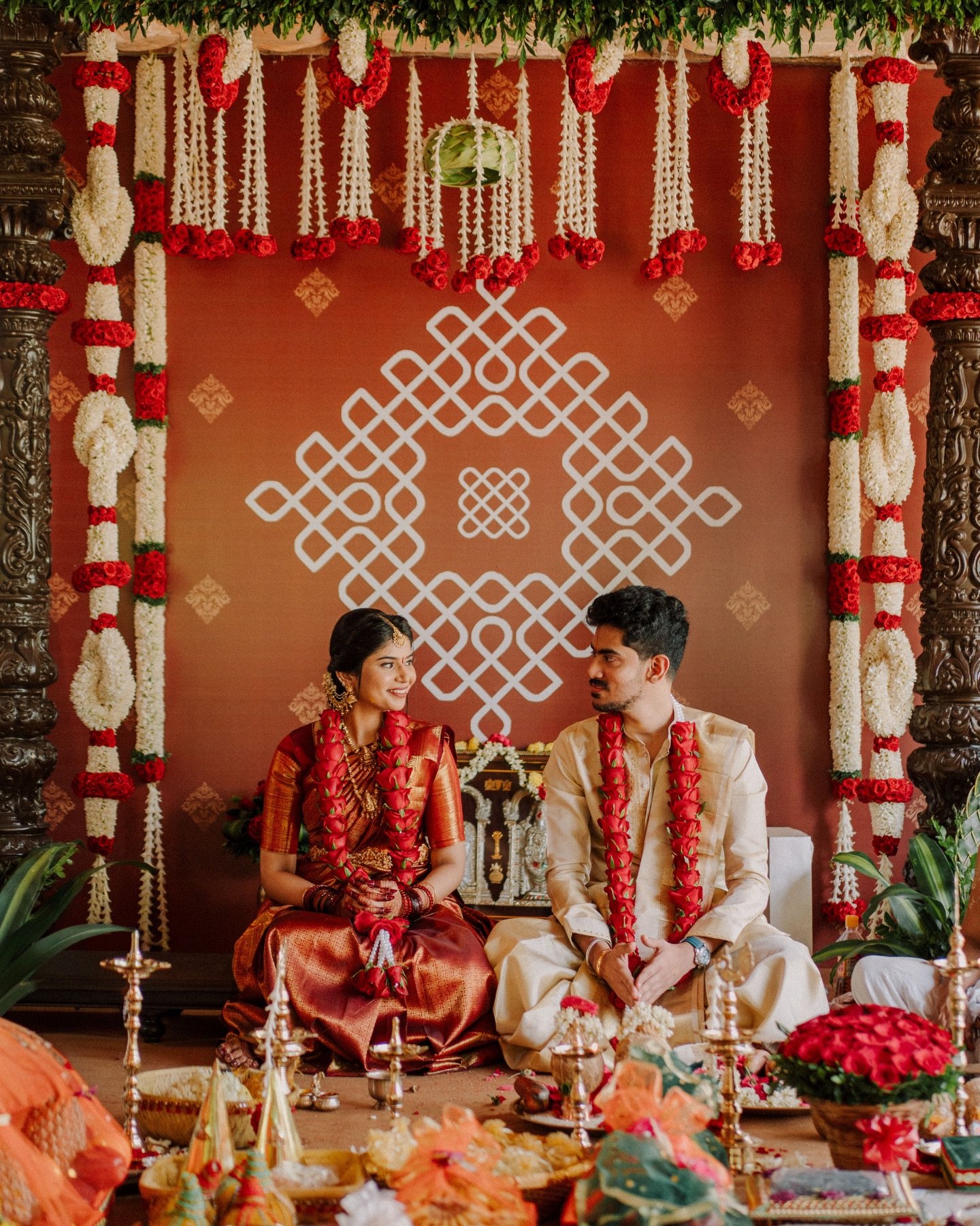 A newlywed couple seated beneath red and white flowers